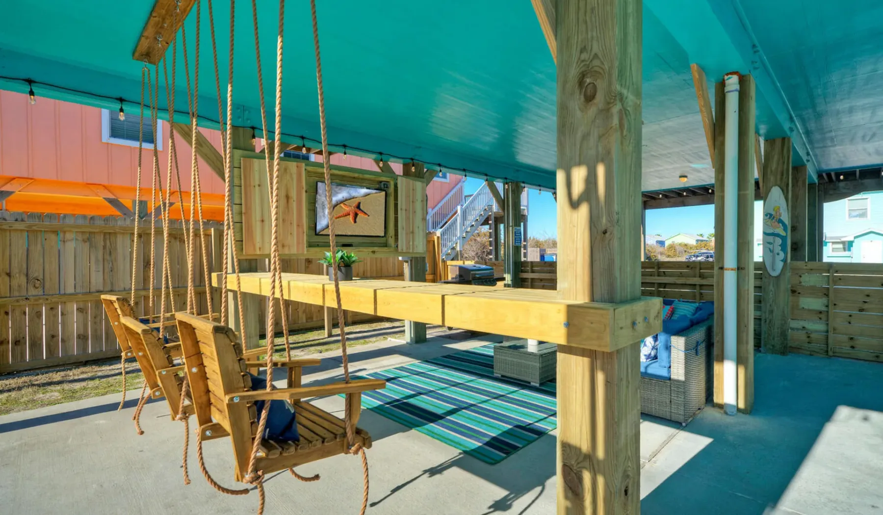 A covered outdoor dining area with wooden seating beside a striped rug.