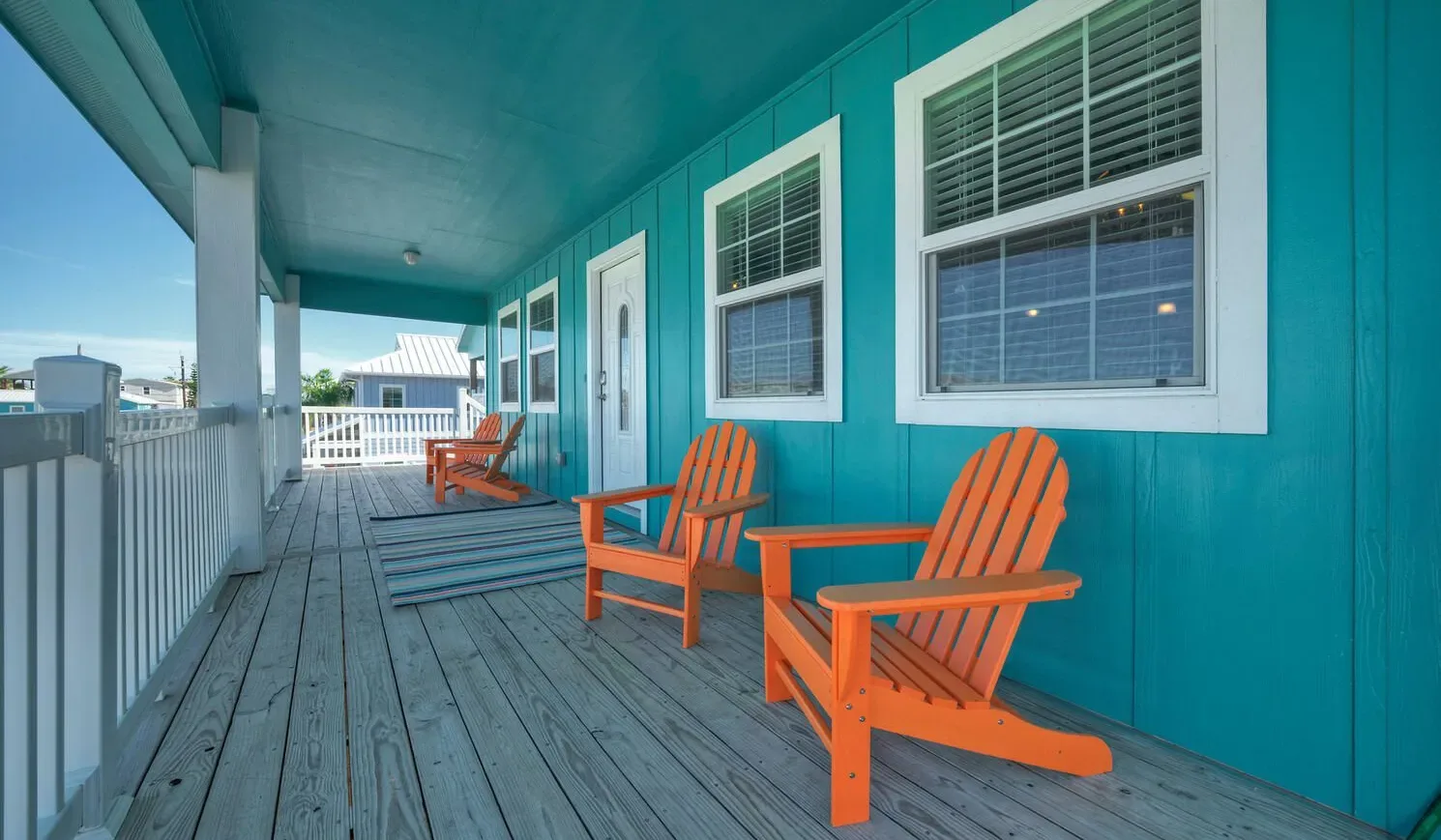 A covered porch with orange seating and a wooden deck beside a turquoise wall.