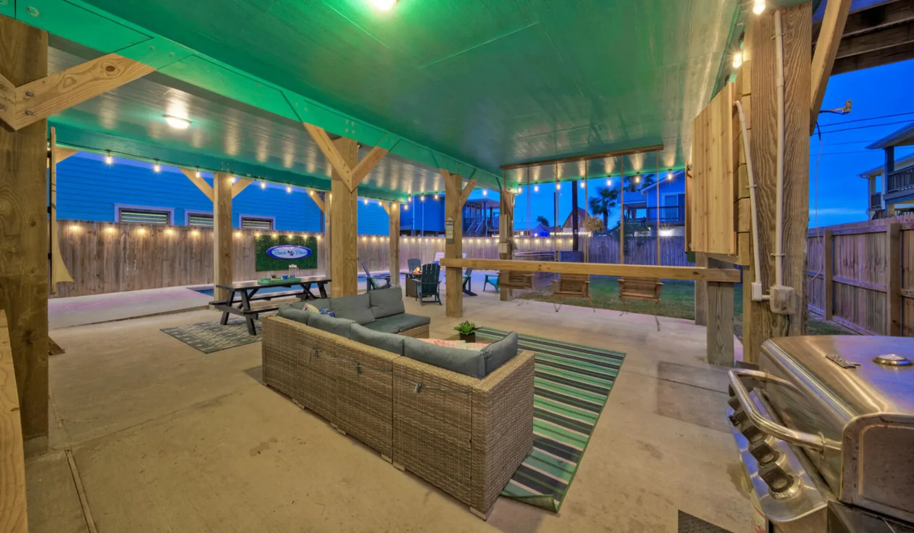 A covered outdoor seating area has wicker seating, a table, and string lights.