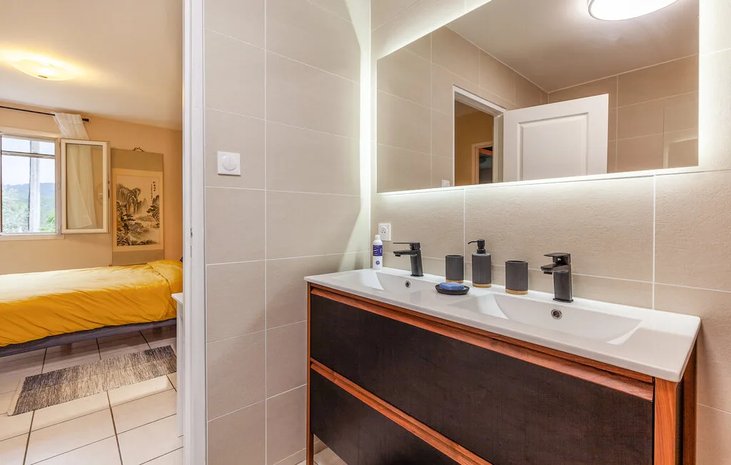 A bathroom vanity with a wide mirror beside a bedroom with yellow bedding.