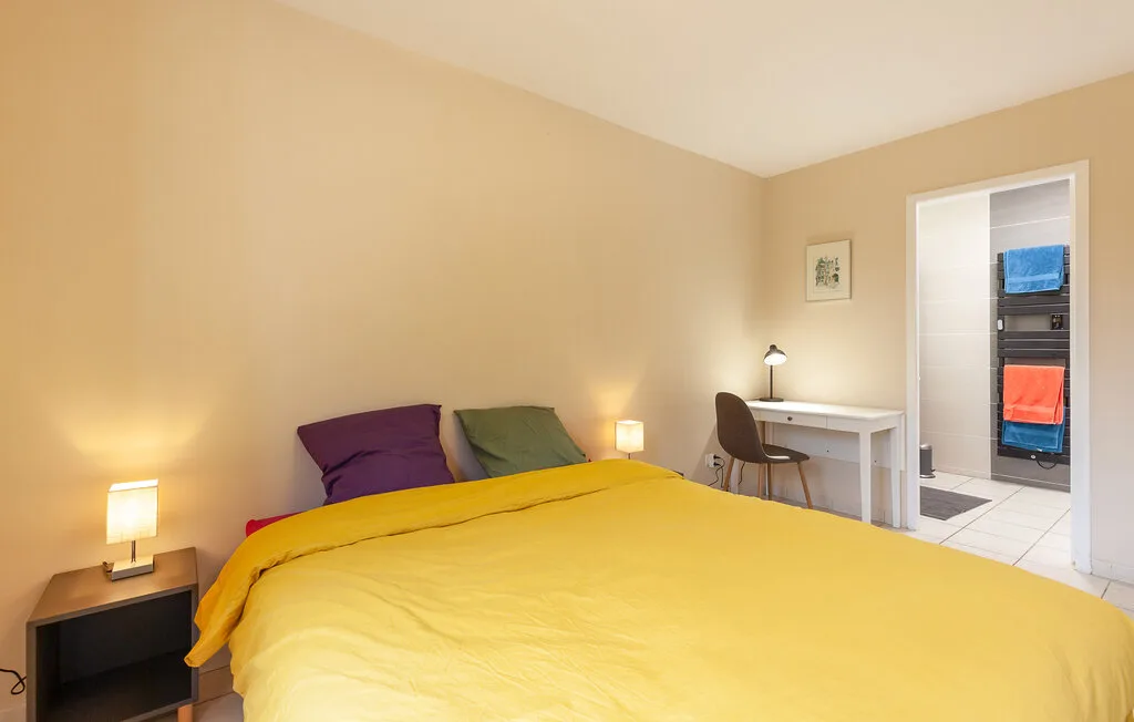 A bedroom with a yellow bedspread and a small desk beside the bed.