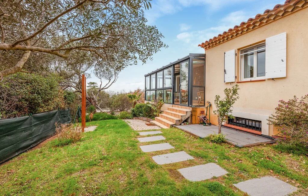 A grassy garden path leads to a glass-enclosed patio beside a house.