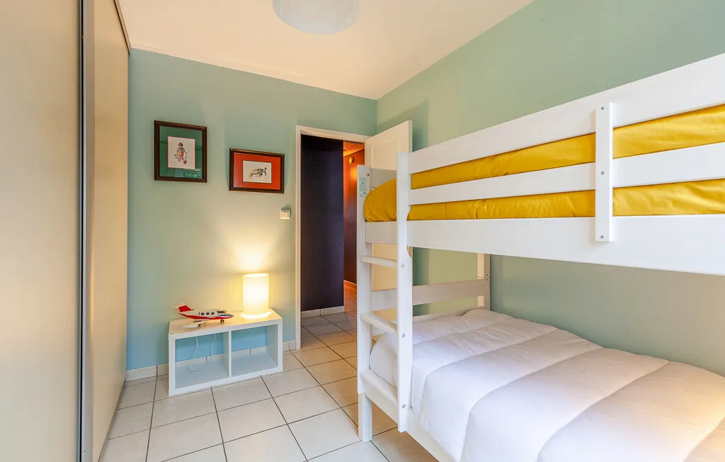 A bunk-bed bedroom with white bedding, pale green walls, and framed pictures.