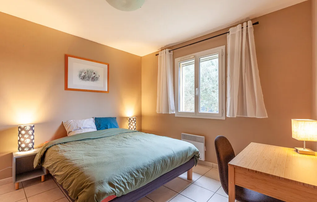 A bedroom with a bed beneath a window and light curtains.