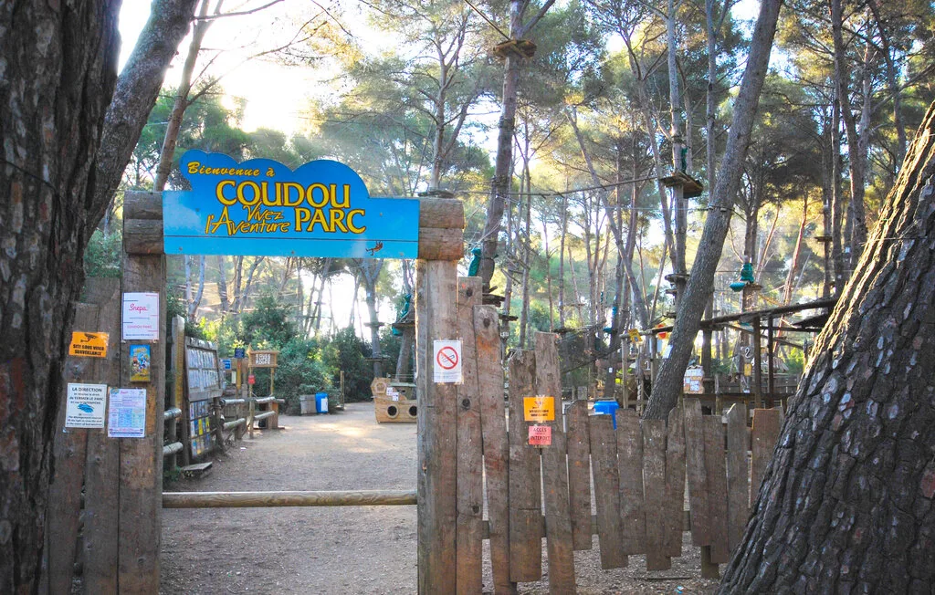 A wooden entrance gate opens onto a path through a wooded park.