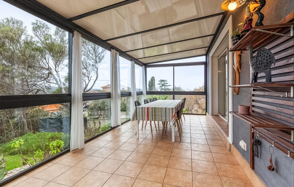 A glass-enclosed dining area with a table overlooking trees.