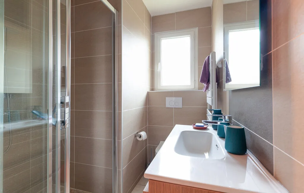 A bathroom with a glass shower and a sink beneath the window.