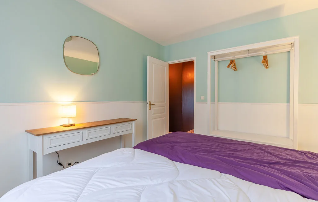 A bedroom with a bed, a desk, and a wall mirror.