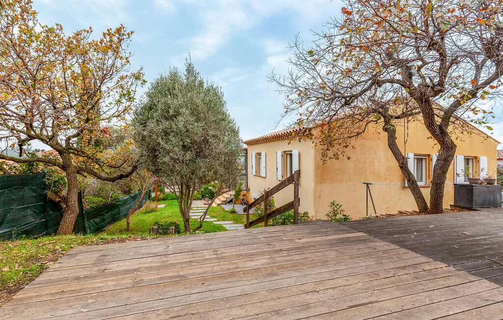 An outdoor wooden deck beside a stucco house and leafy trees.