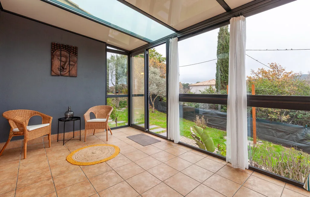A bright enclosed patio with wicker seating and windows overlooking a garden.