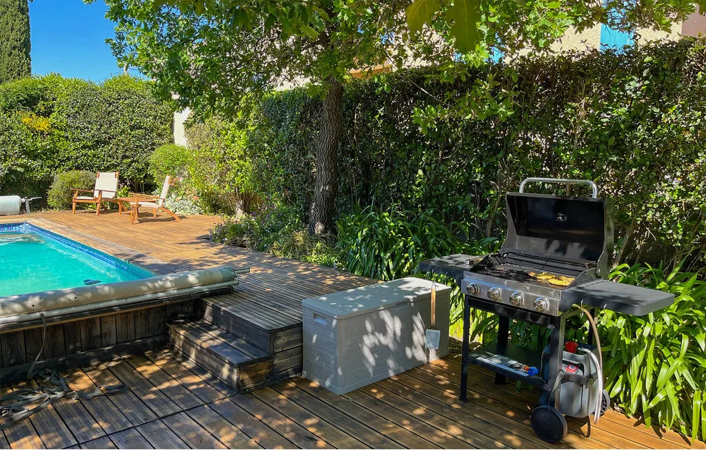 An outdoor pool deck with a barbecue grill beside the water.