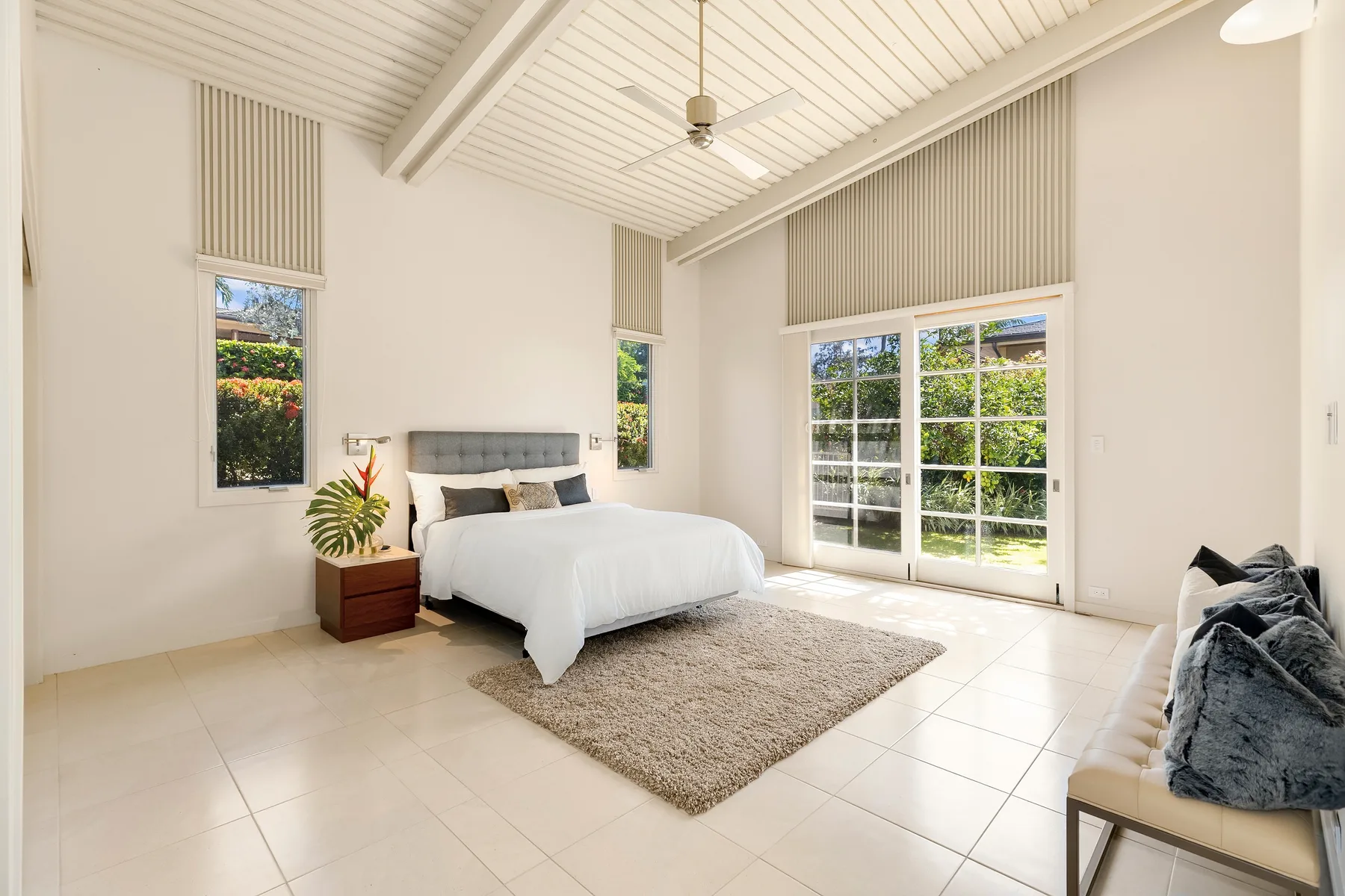 Un dormitorio luminoso con una cama, ventanas grandes y puertas corredizas de vidrio.