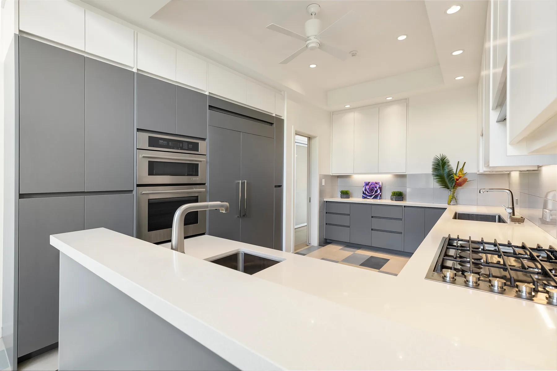 Una cocina moderna y luminosa con gabinetes grises, hornos empotrados e isla blanca.