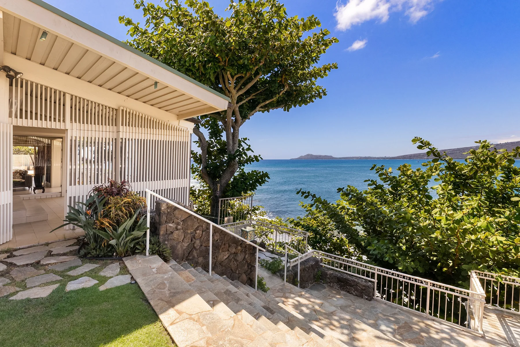 Una terraza junto al mar mira hacia el agua, con escalones y vegetación en primer plano.