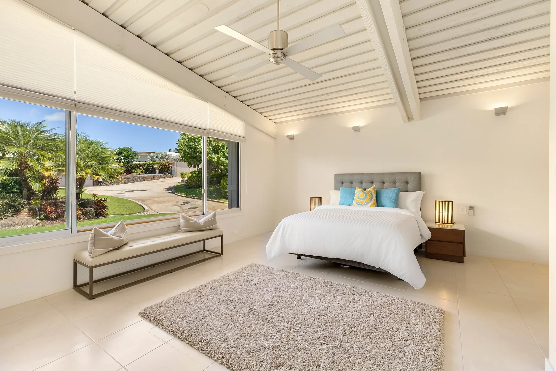 Un dormitorio luminoso con una cama bien tendida y grandes ventanas con vistas a la vegetación.