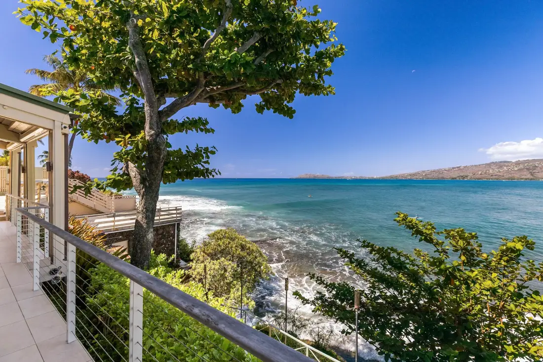 Una terraza junto al mar mira al agua turquesa, con un árbol frondoso junto a la barandilla.