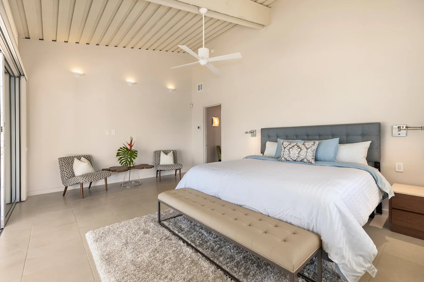 Un dormitorio luminoso con una cama grande, un banco y una pequeña zona de estar.