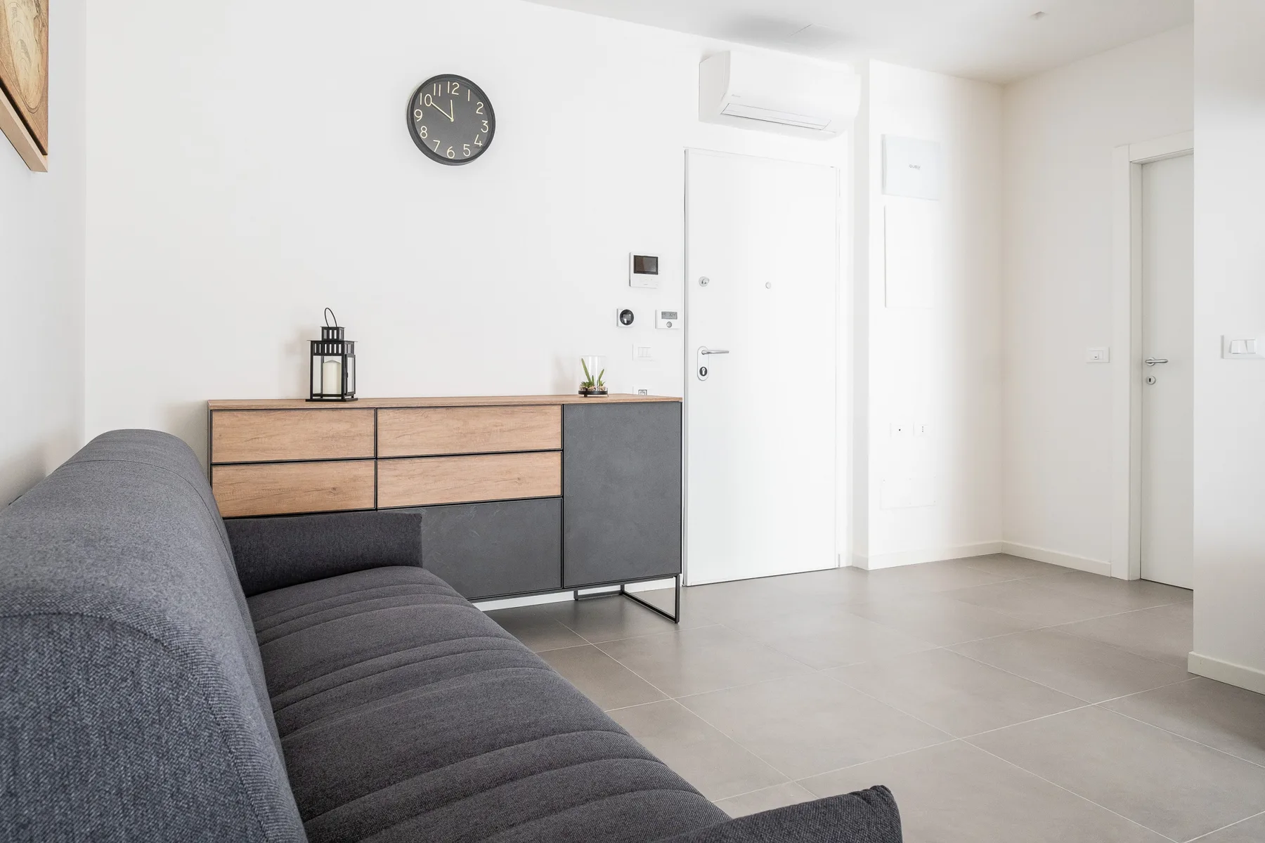 A bright living room with gray seating and a wood-front cabinet.