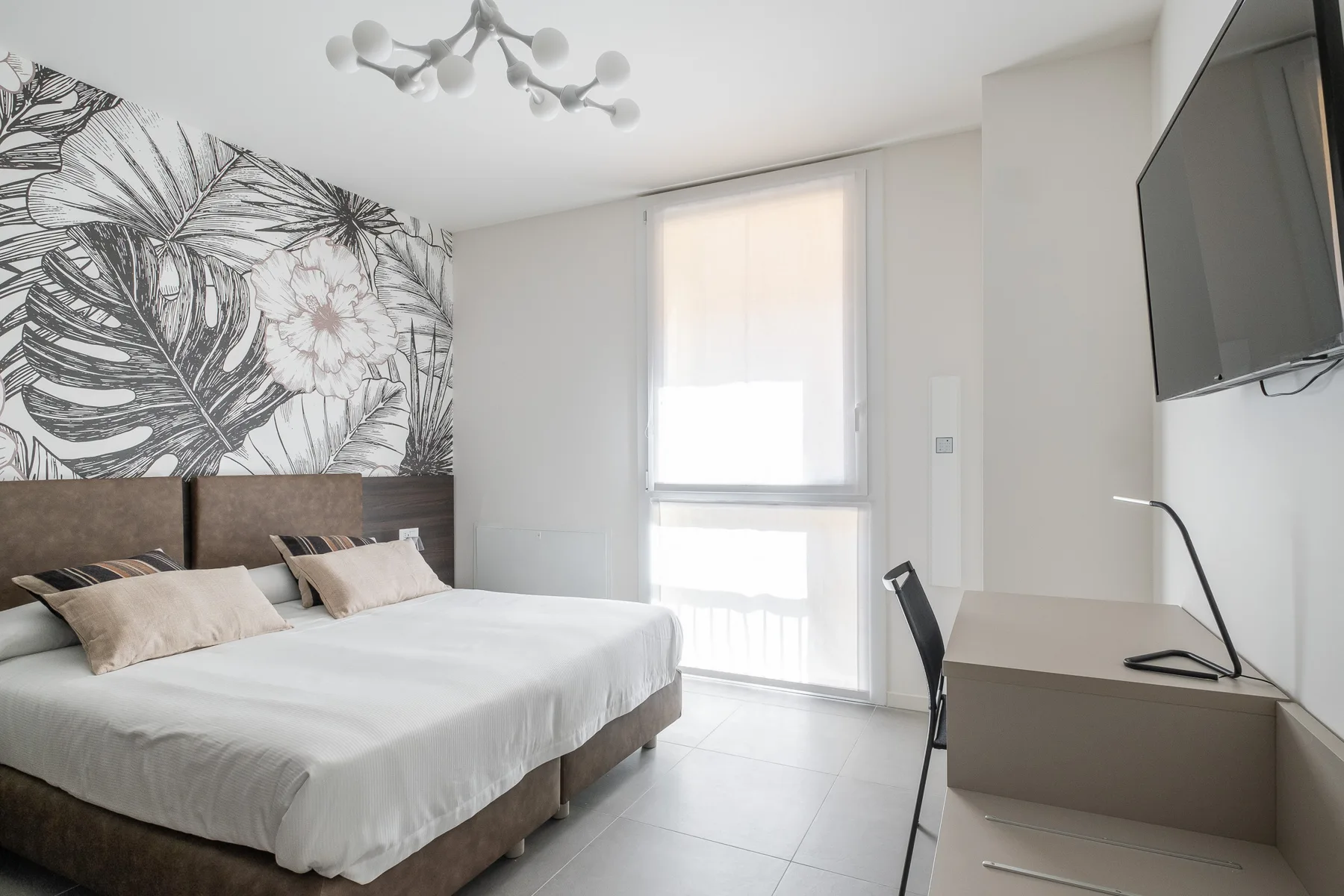 Un dormitorio luminoso con una cama, un mural botánico y un escritorio.