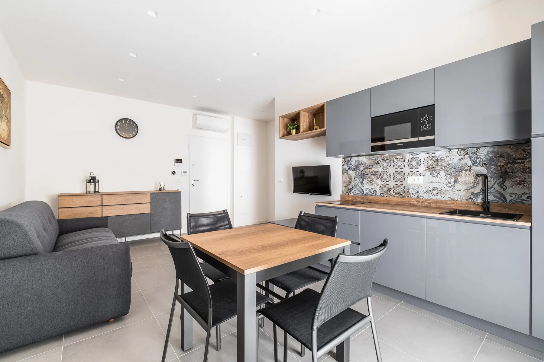 Cocina y comedor modernos con gabinetes grises y una mesa de madera.