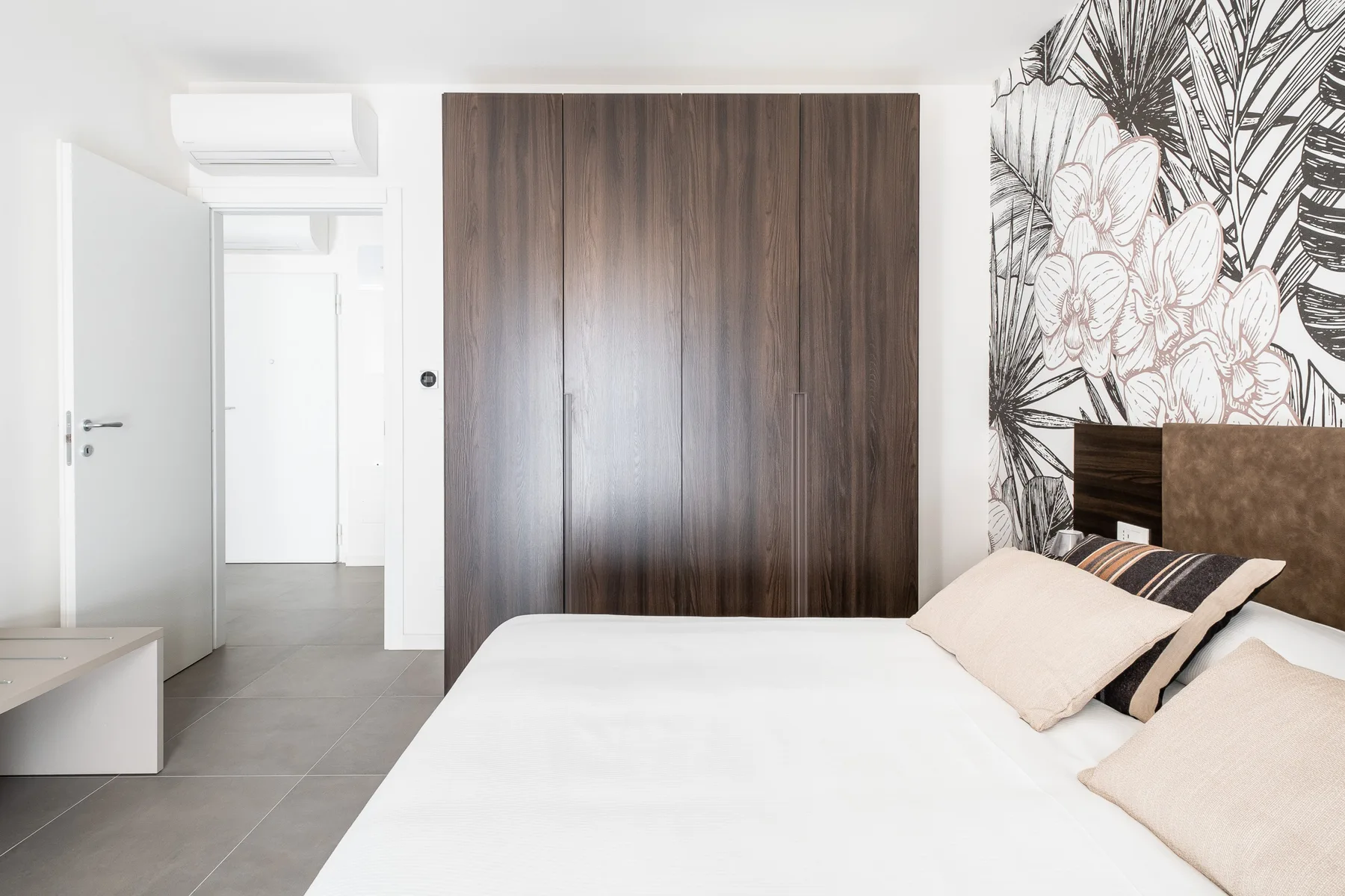 Un dormitorio con una cama tendida, un armario oscuro y un mural floral.