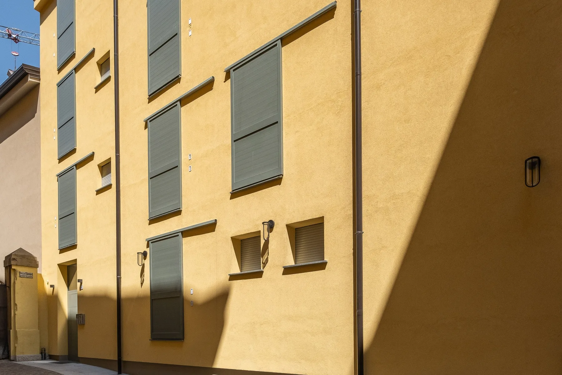 Una fachada amarilla con varias ventanas con persianas bajo la luz del sol.