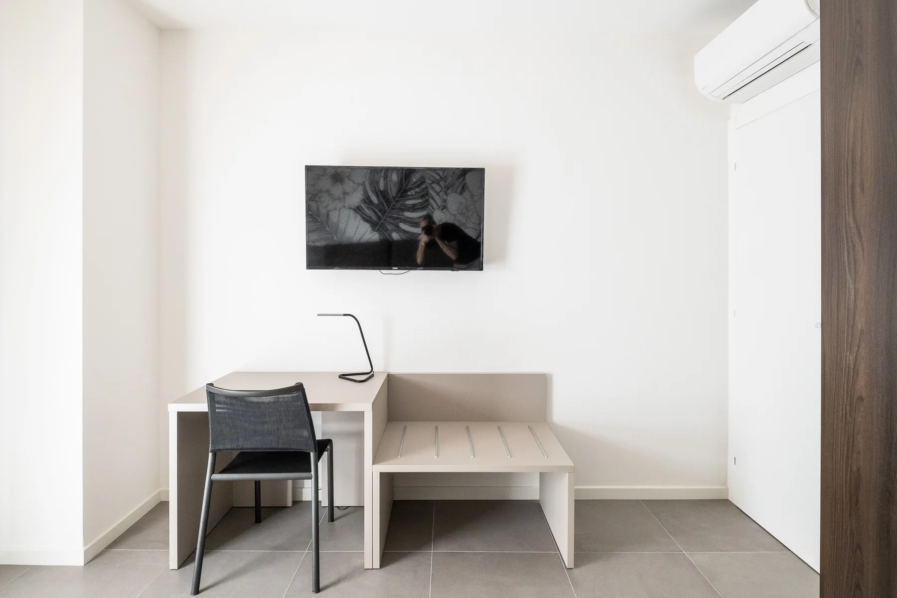 Un espacio de trabajo luminoso con escritorio, silla y mesa baja bajo una pantalla en la pared.