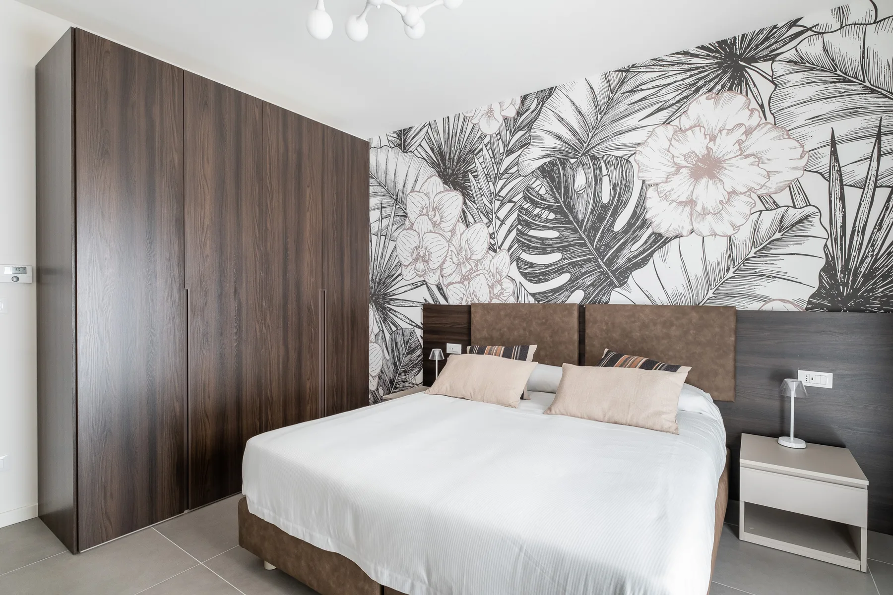 A bedroom with a white bed and large floral wall mural.