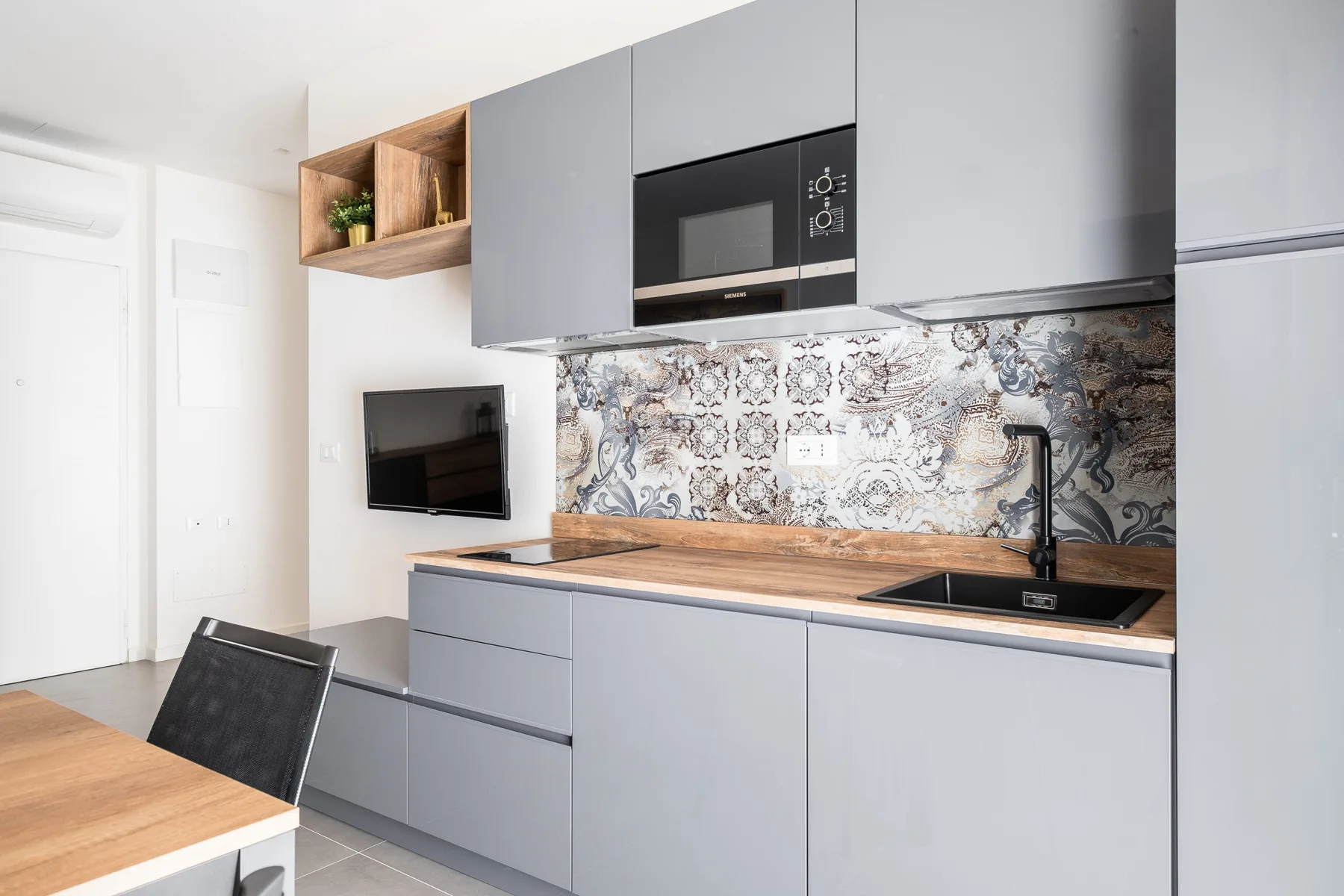 Una cocina moderna con gabinetes grises, un salpicadero estampado y una encimera de madera.