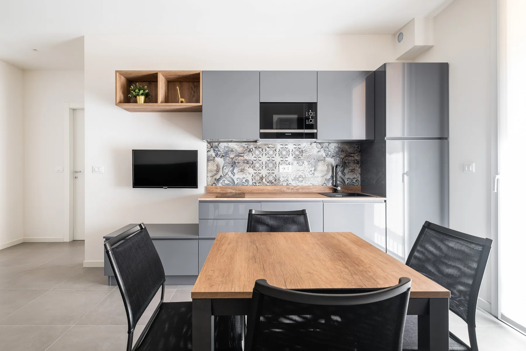 Una mesa de comedor y asientos miran hacia una cocina compacta con salpicadero estampado.
