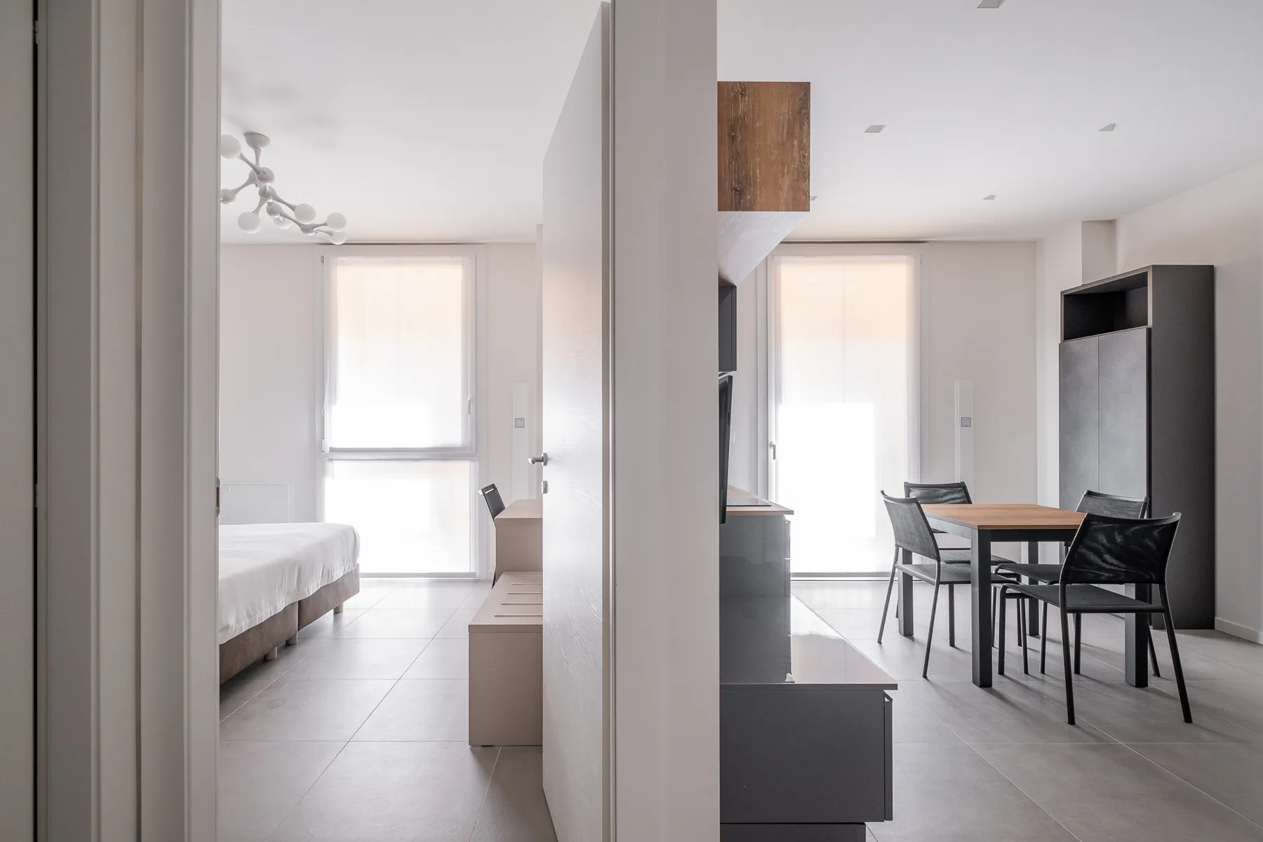Una habitación luminosa y diáfana con cama, mesa de comedor y ventanales.