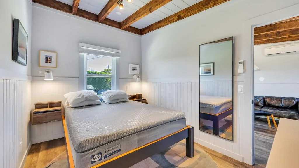 A bright bedroom with a bed beneath exposed wooden ceiling beams.