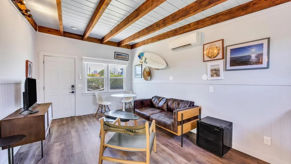 A living room with seating, a television, and exposed wooden ceiling beams.
