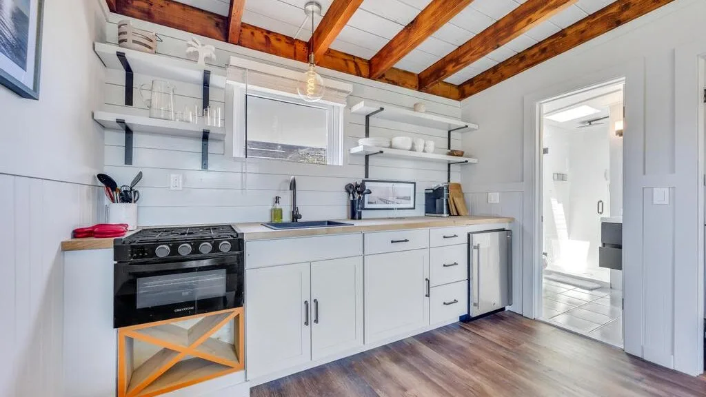 A bright kitchen with white cabinets, open shelves, and exposed wooden ceiling beams.
