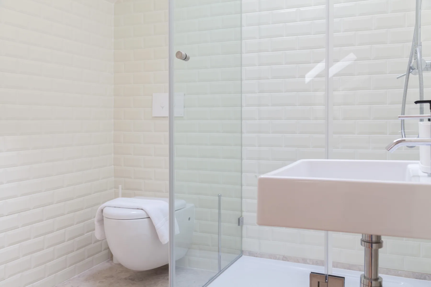 A bright bathroom with a toilet, glass shower, and wall-mounted sink.