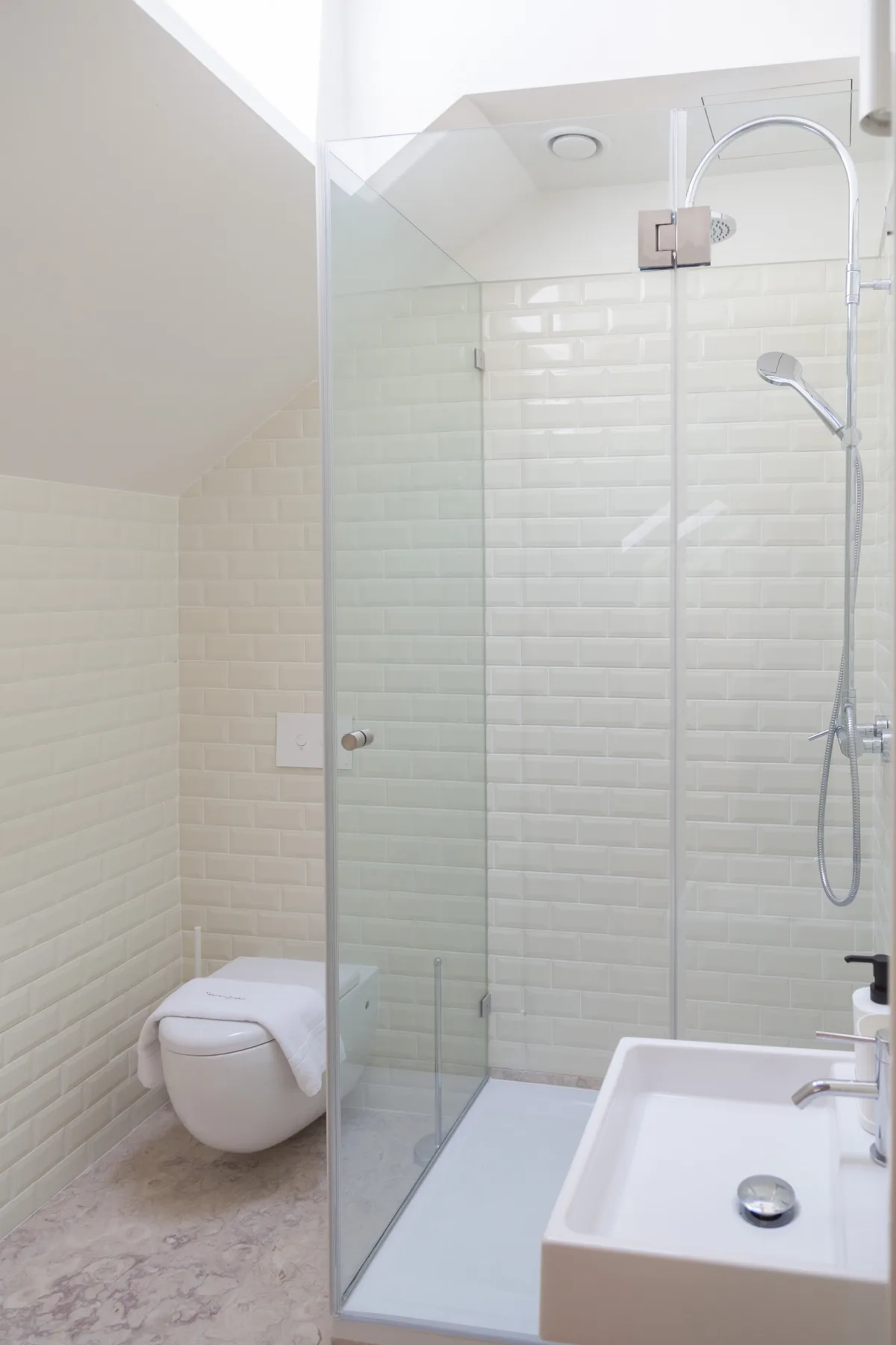 A bright bathroom with a glass shower, wall-mounted toilet, and sink.