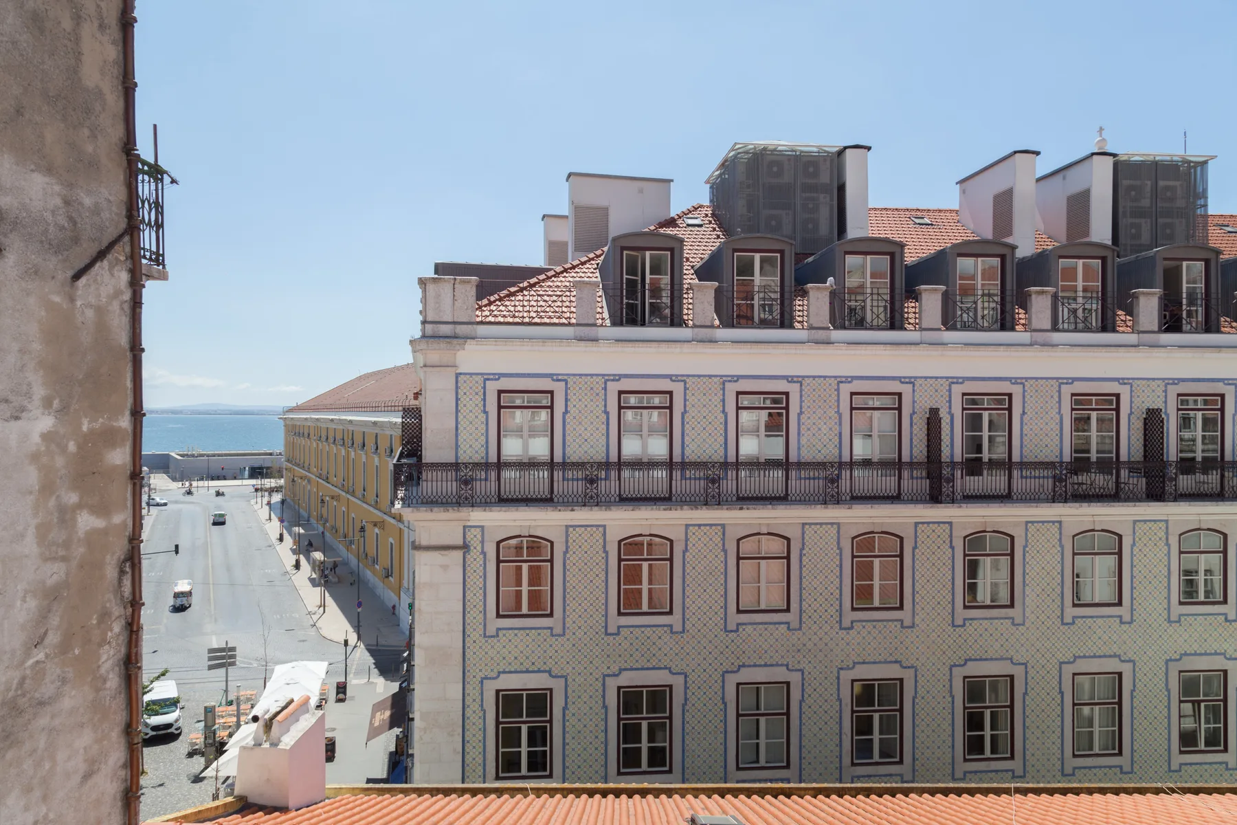 A city street beside a multi-story building, with the waterfront visible in the distance.