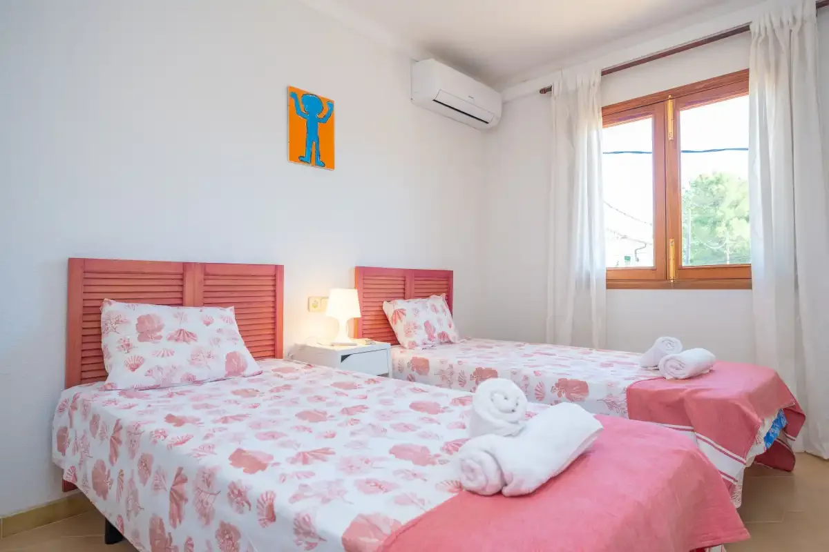 A bright bedroom with two beds, floral bedding, and a window.
