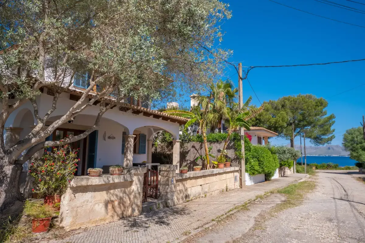 A Mediterranean-style house with a stone wall sits beside a quiet road.