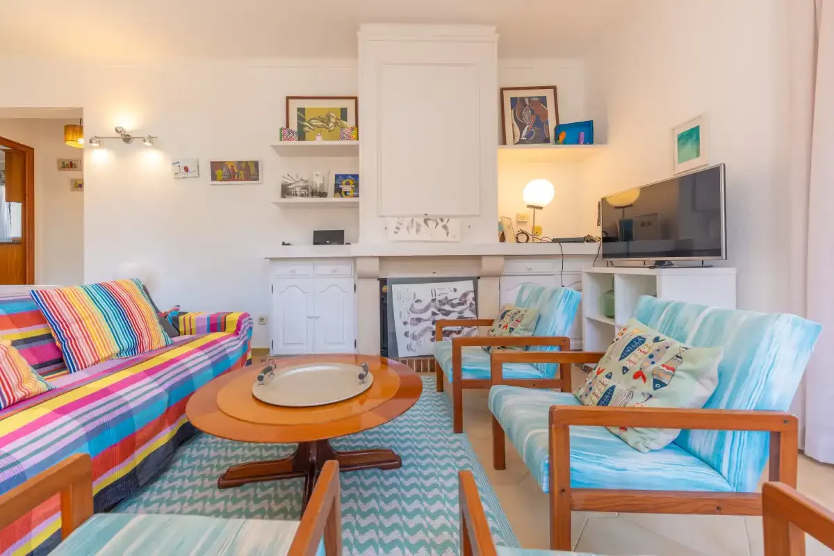 A bright living room has colorful seating, a round coffee table, and a television.