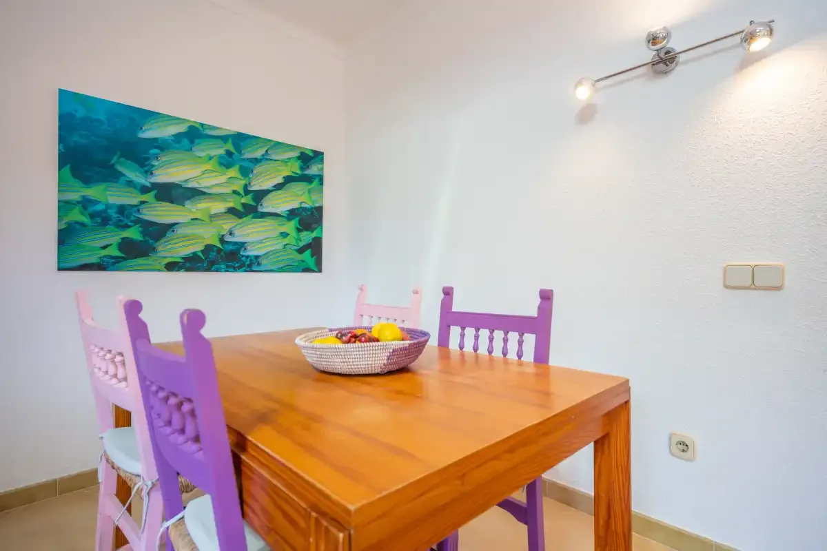 A dining area with a wooden table, purple chairs, and colorful fish artwork.