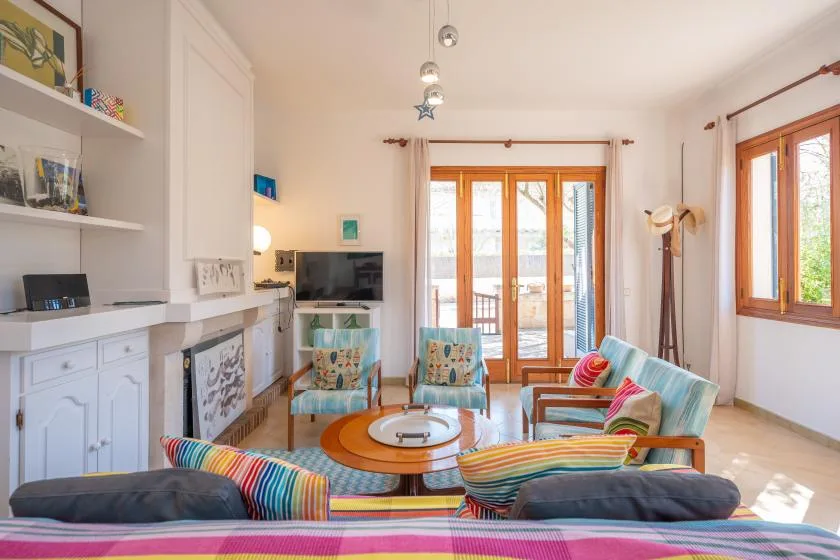 A bright living room with colorful seating and large wooden-framed windows.