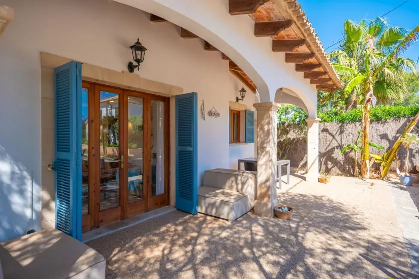 Un patio cubierto y soleado con puertas de vidrio, contraventanas azules y asientos al aire libre.