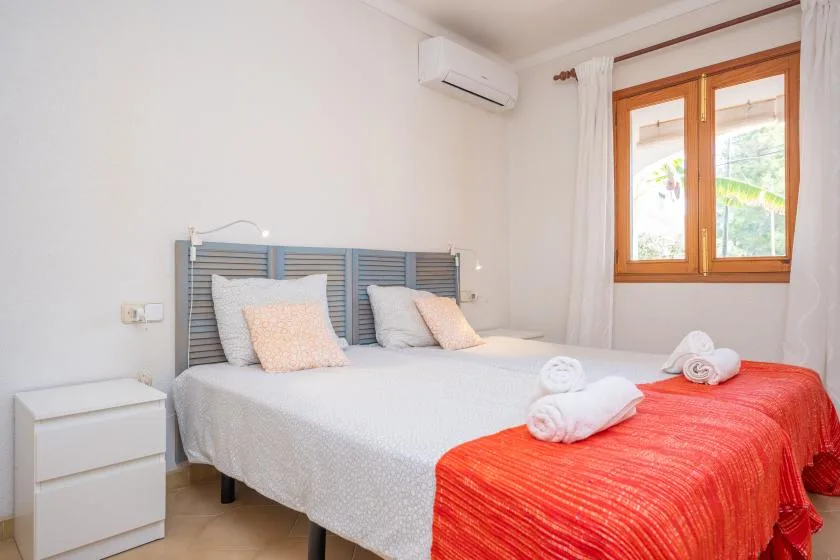 A bedroom with a double bed, red bedspread, and a window with curtains.