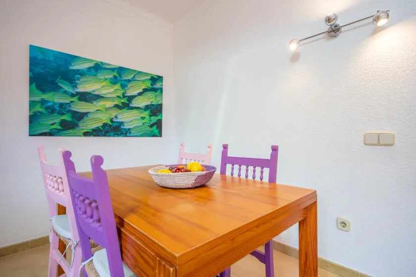 A wooden dining table with purple seating sits beneath a colorful fish painting.