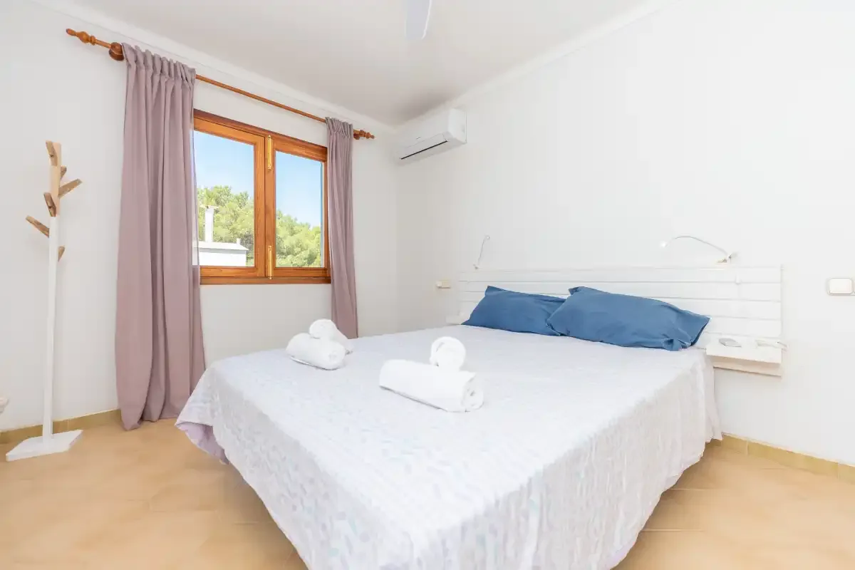A bright bedroom with a bed and a window framed by curtains.