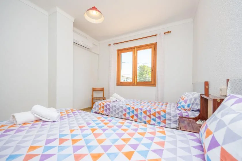 A bright bedroom with colorful patterned bedding and a wooden-framed window.