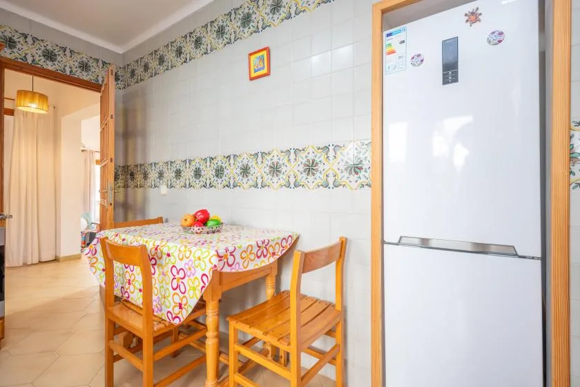 A tiled dining area with a table, wooden chairs, and a refrigerator.
