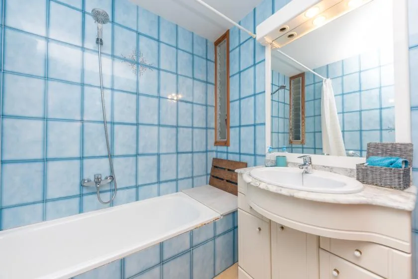 A bathroom with a bathtub, tiled walls, and a sink beneath a large mirror.