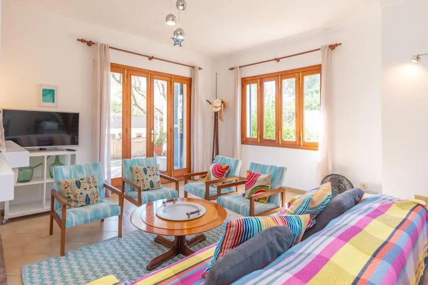 A bright living room with colorful seating and large wood-framed windows.